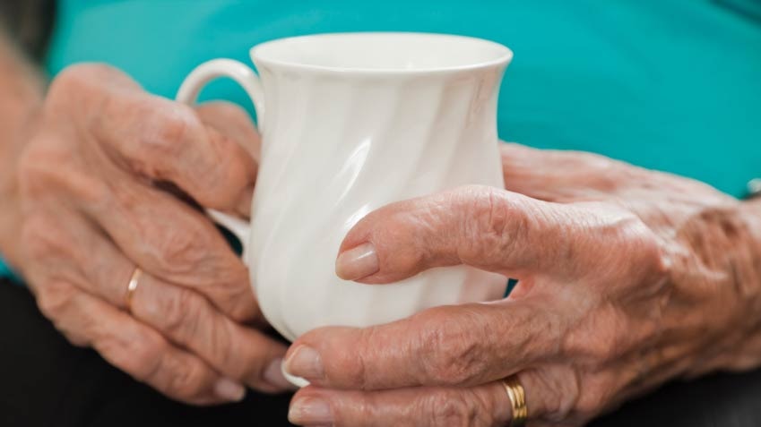 A close-up of an older person's hands gripping a tea cup