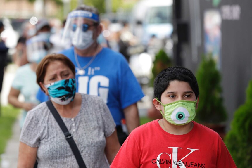 People wear different coloured masks as they wait in a line outside.