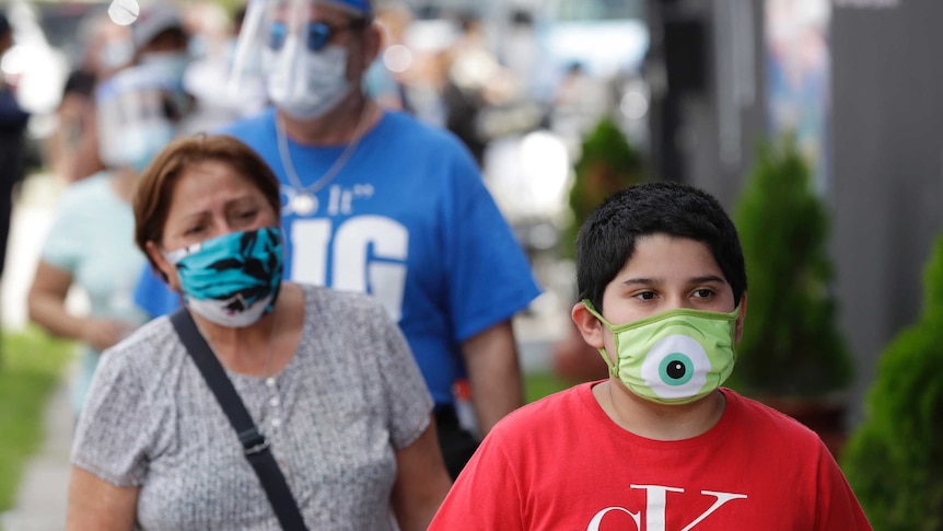 People wear different coloured masks as they wait in a line outside.