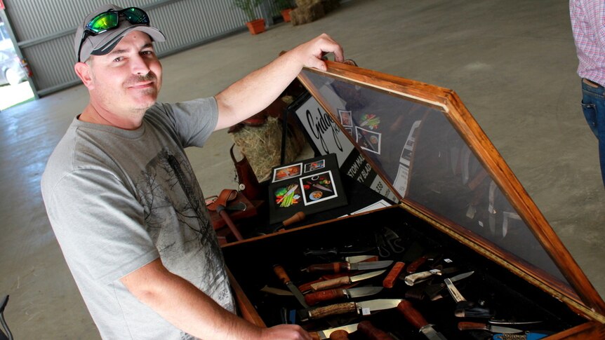 Bundaberg knife maker Scott Simmonds stands beside an open case displaying his hand made knives