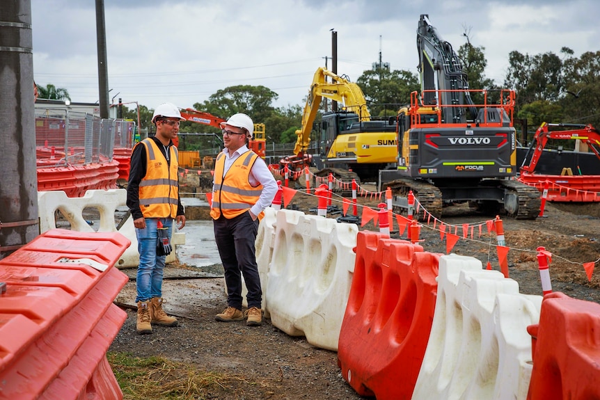 Two men wearing hard hats and hi vis talking to each other at a construction site.