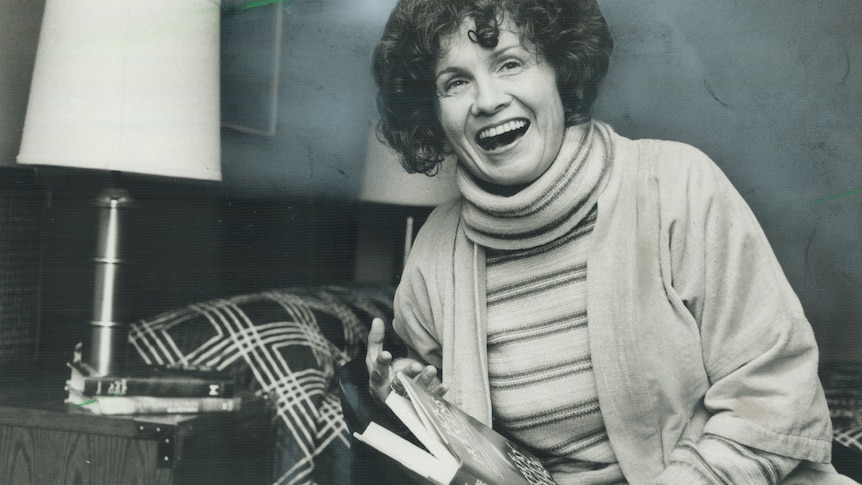 A black and white photograph of a woman laughing while holding a book.