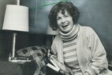 A black and white photograph of a woman laughing while holding a book.
