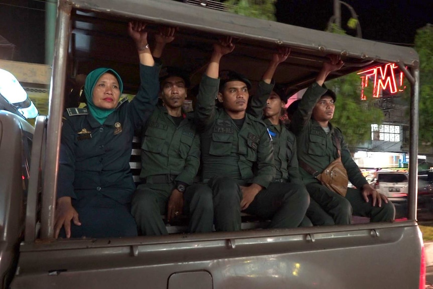 Fou male officers and a female officer sit in the back of an open patrol vehicle