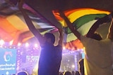 Two men sit on other peoples' shoulders and wave two rainbow flags at a concert in Cairo.