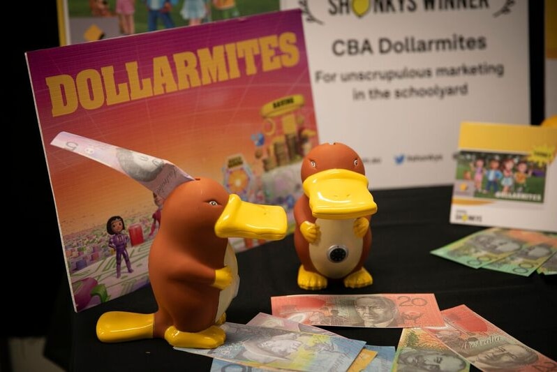 Two platypus moneyboxes with five, ten and twenty dollar notes around them and an award certificate in background.
