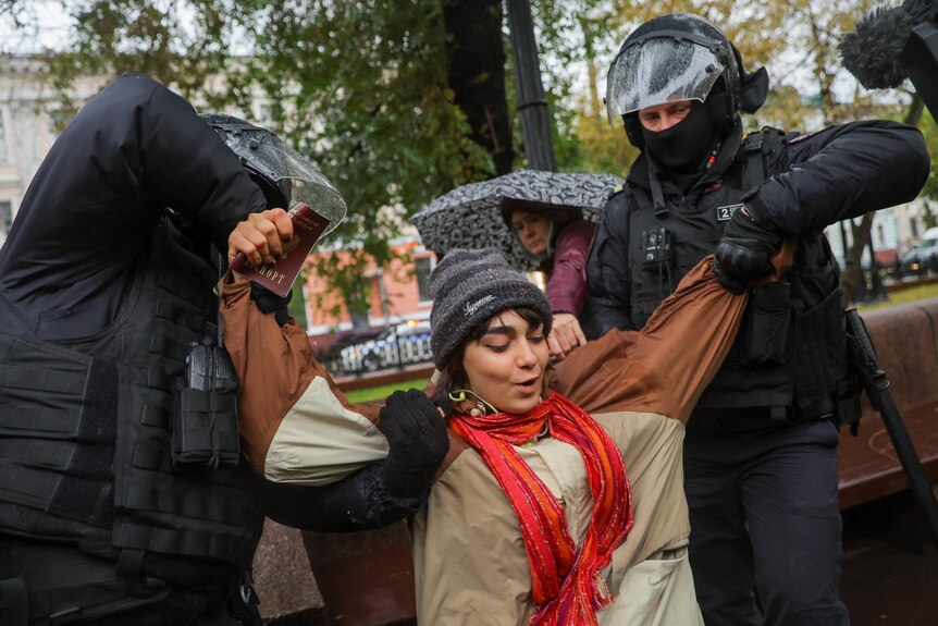 Two riot police officers pull at the clothing of a woman during an arrest at an anti-war rally.