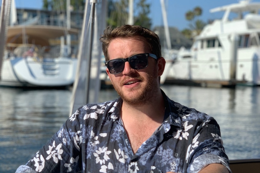 Man wearing a blue printed shirt, sitting by the water. 