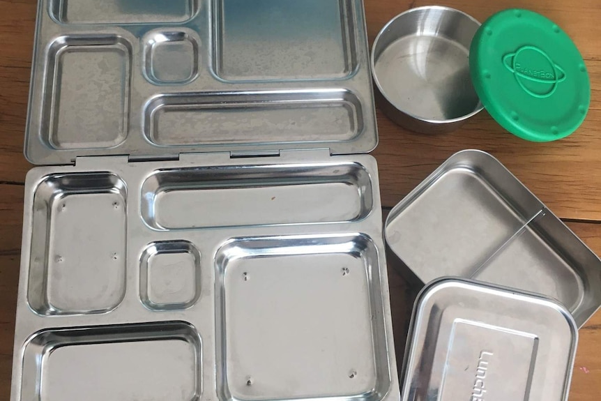 A metal lunchbox with four separate compartments with two small metal containers next to it
