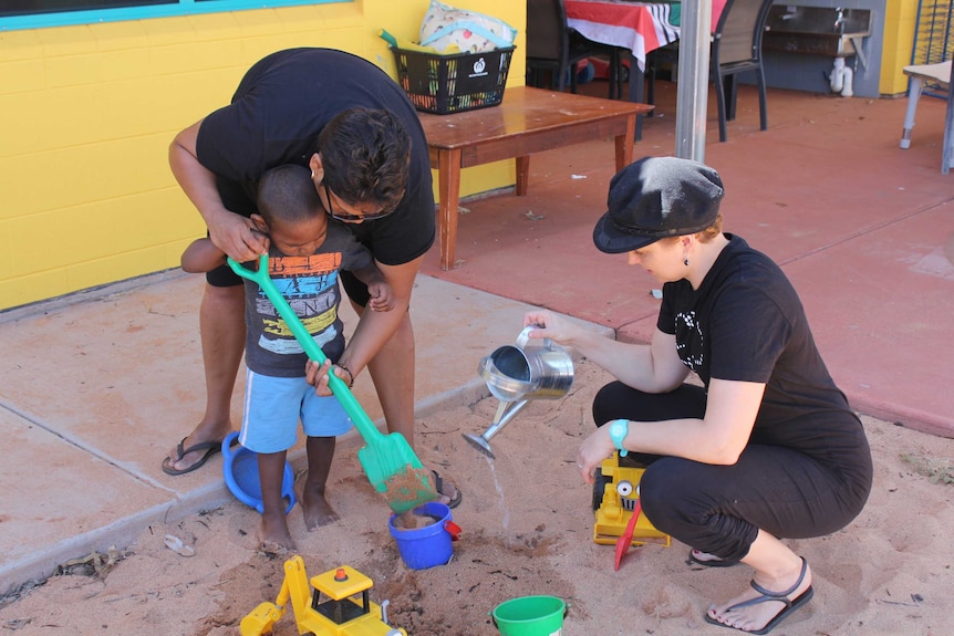 Two women play in a sandpit with a young Indigenous boy.