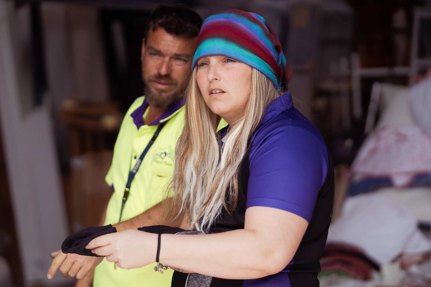 A side-on shot of Dee Freitag standing next to a man in a high-vis yellow work shirt.