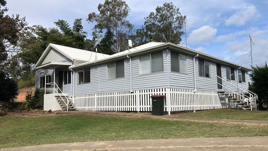 A large, freshly painted, grey and white Queenslander-style farmhouse.
