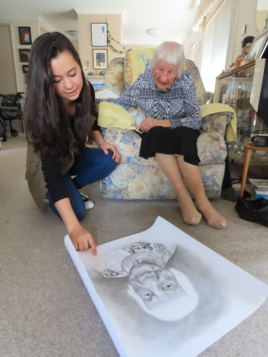 Hasinah Zainal shows Peggy Muller her portrait in progress rolling the sketch out on the floor.