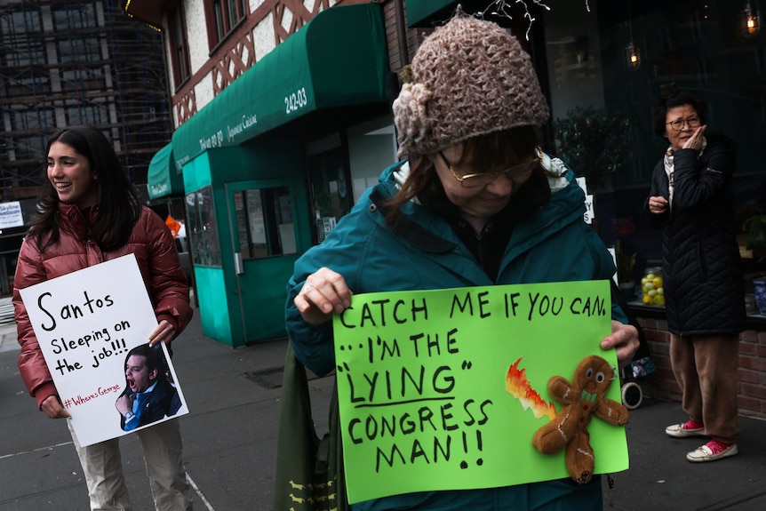 A woman holds a green cardboard sign saying 'Catch me if you can, I'm the lying congressman!!!' with a gingerbread man on it