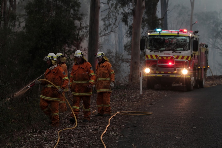 Four firefighters with a fire truck on a road.