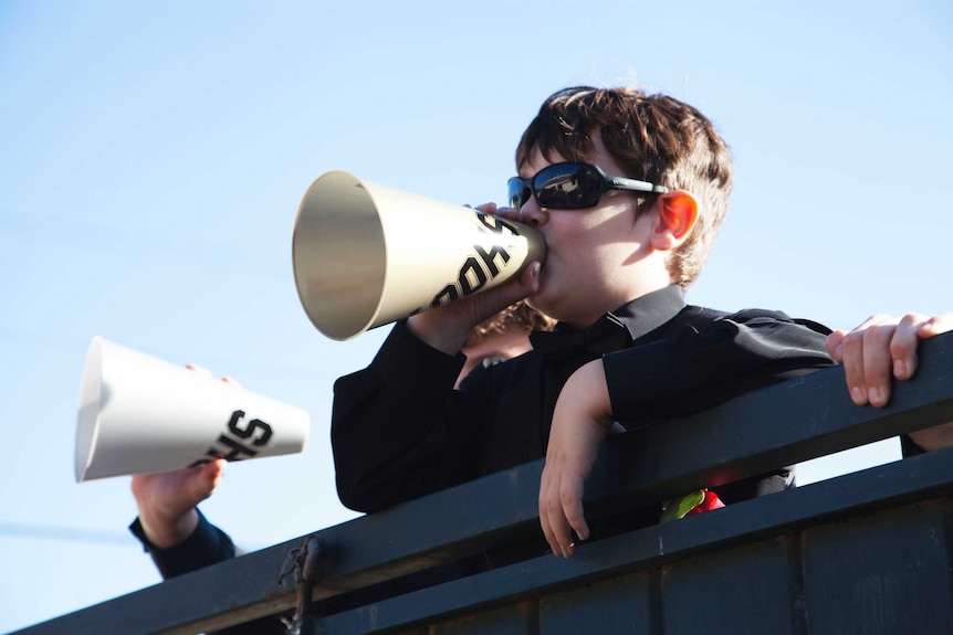 A young boy in sunglasses yells through a megaphone