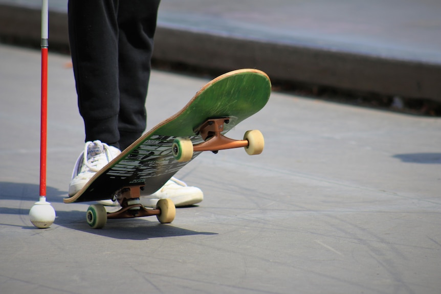 A person's feet on a skateboard beside a cane. 