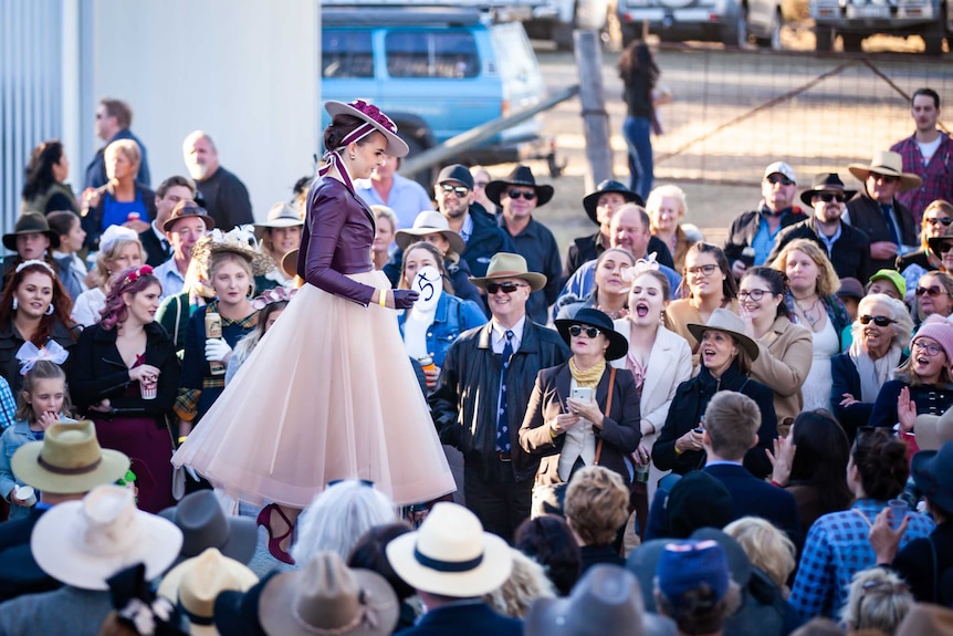 A woman in the fashions on the field competition walks the runway with a packed crowd around her watching.