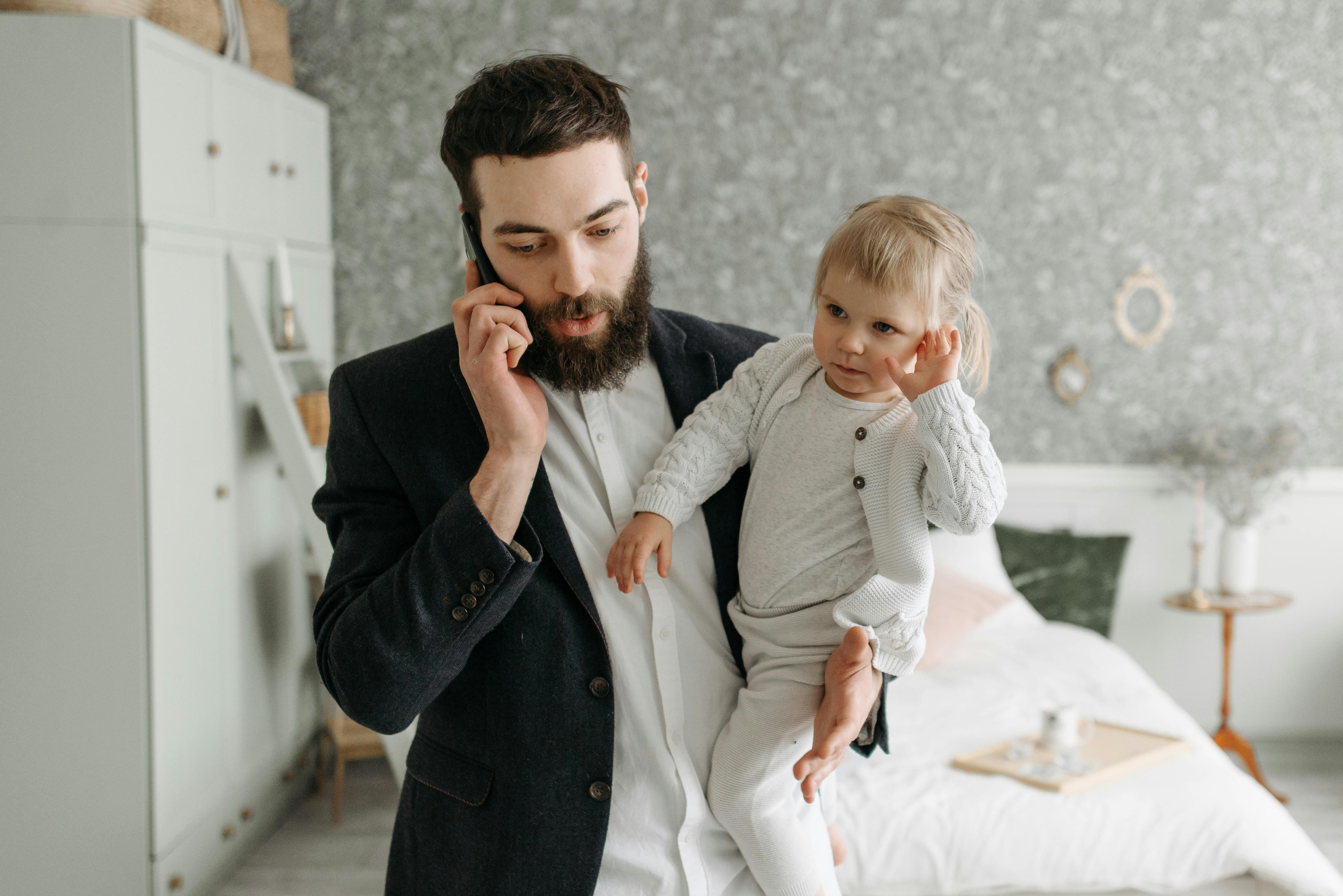 dad on phone while holding his toddler