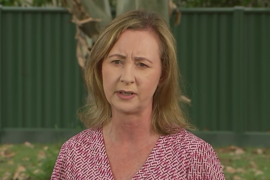 Yvete D'Ath standing outside in a red and white top, speaking, looking concerned