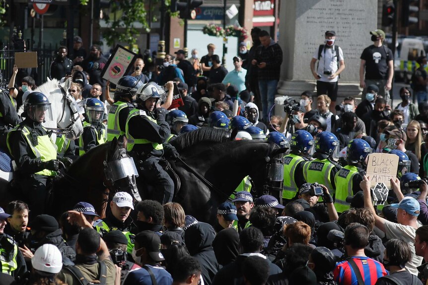 British mounted police officers ride through a thick crowd of protesters.