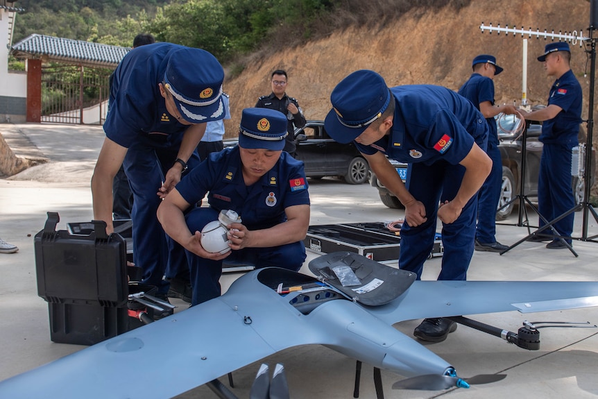 三个穿着蓝色制服的男人蹲在一架无人机周围。