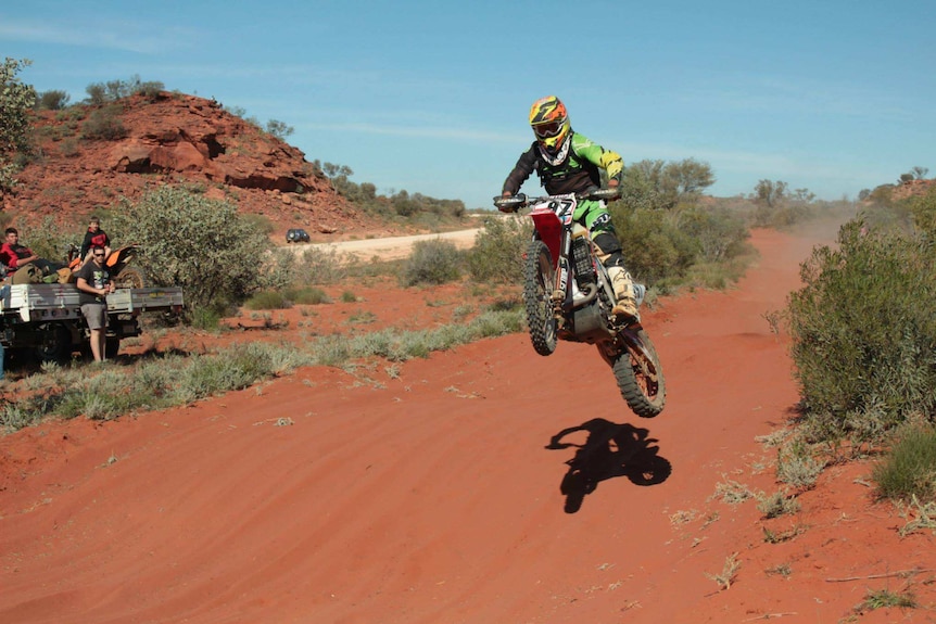 Daymon Stokie racing on his motorbike down a red dirt road.