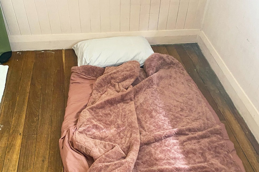 A pillow, mattress and blanket on the floor of a house.