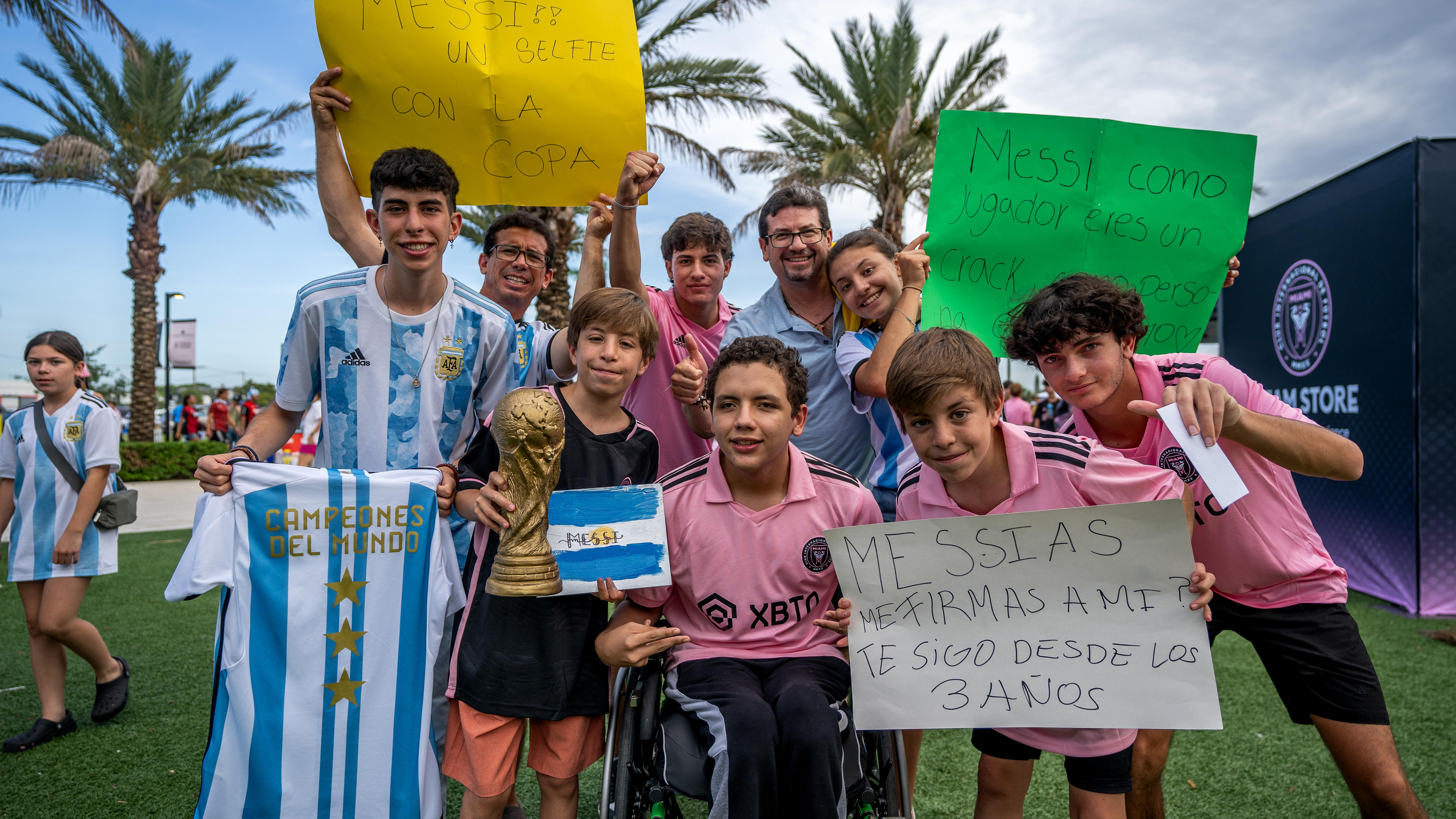 A group of young children with jerseys and signs with messages for Lionel Messi smile together