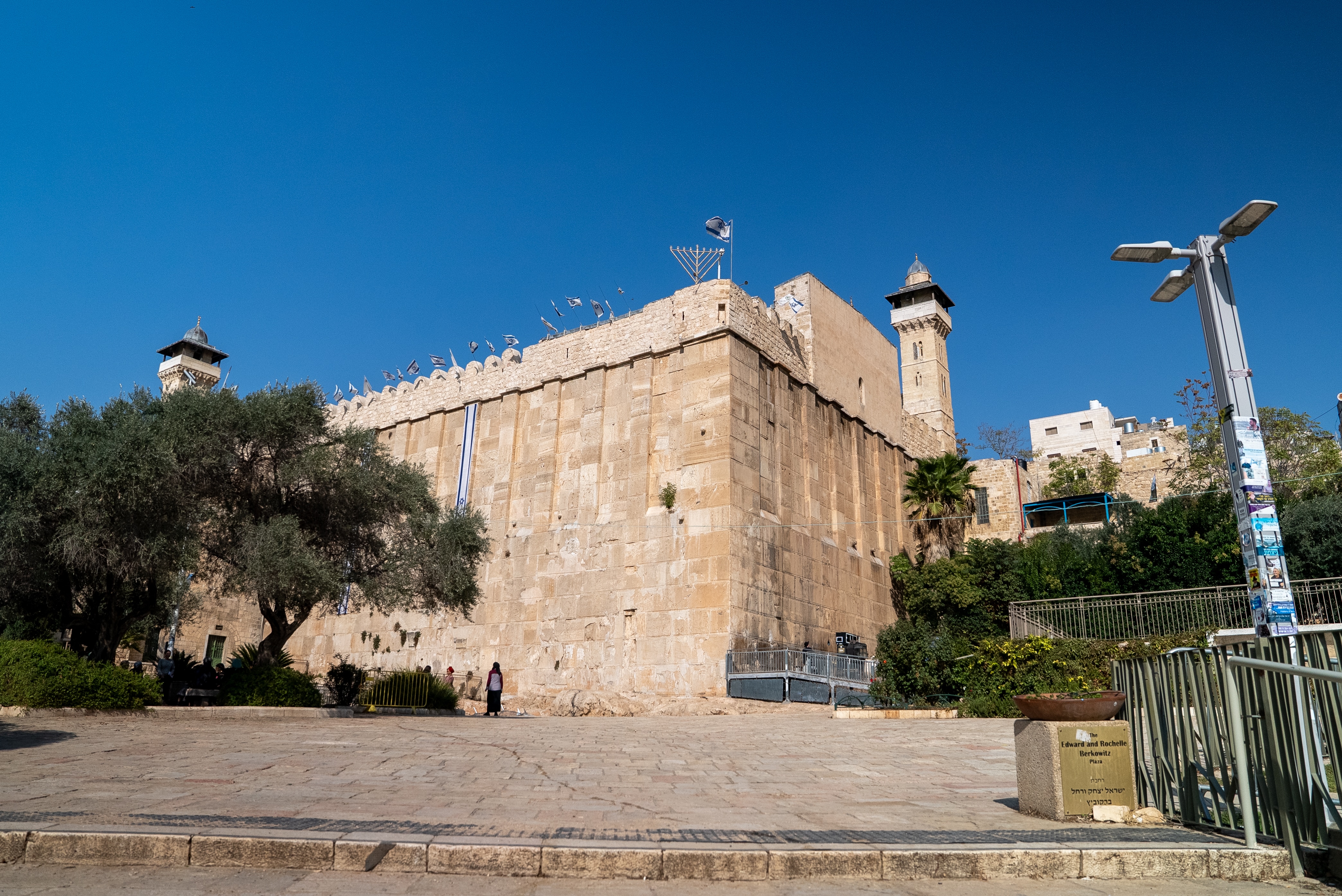 The side of an old building with towers and barbed wire on top 