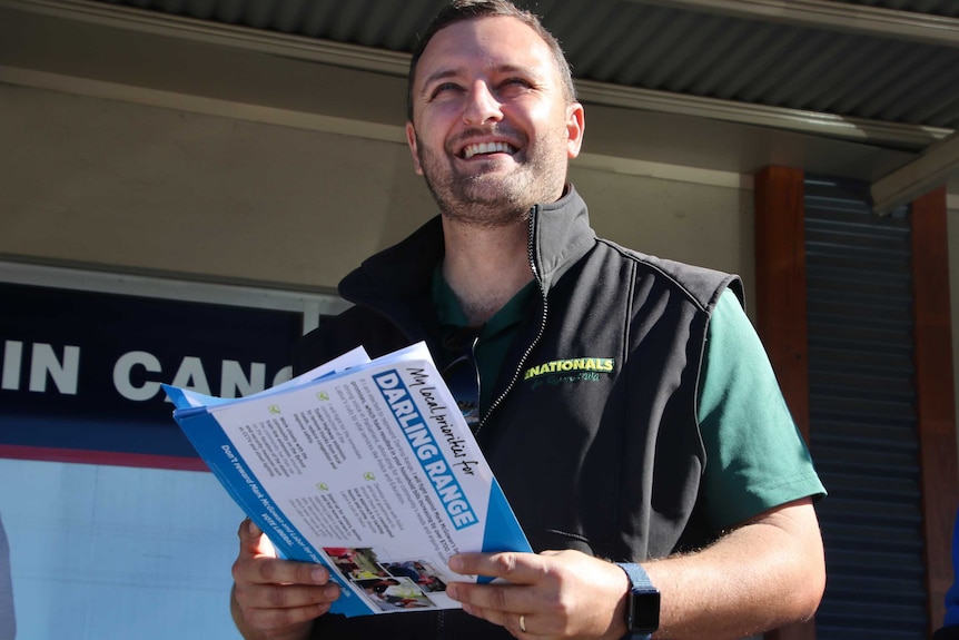 WA Nationals MP Vince Catania stands smiling and holding Liberal how-to-vote cards.