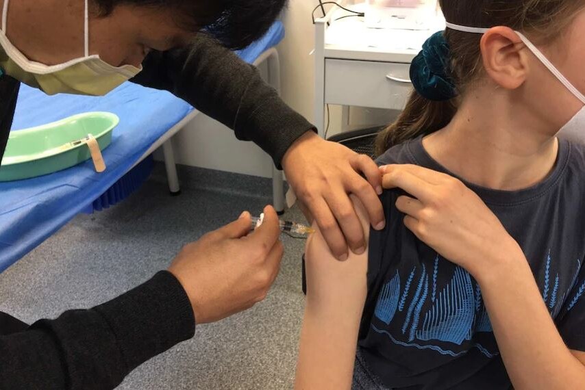Arm of child being injected with COVID-19 vaccination in a doctor's room.