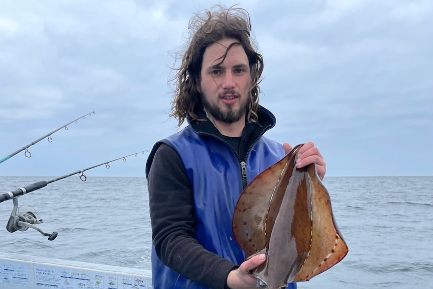 a man standing on a boat wearing waders holds a large squid