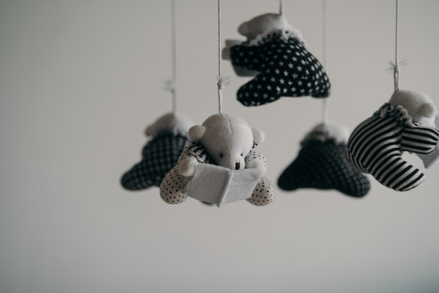 A baby mobile hangs from the ceiling with little teddy bears on them.