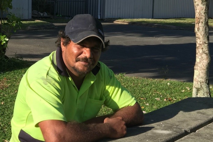 Charles Murgha sits at a picnic table in his high-visibility work gear, smiling.