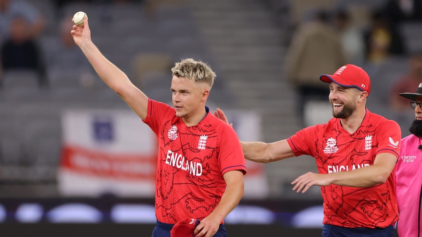 A bowler wearing a red England shirt raises the ball to the crowd after taking five wickets, as a teammate pats him on the back.