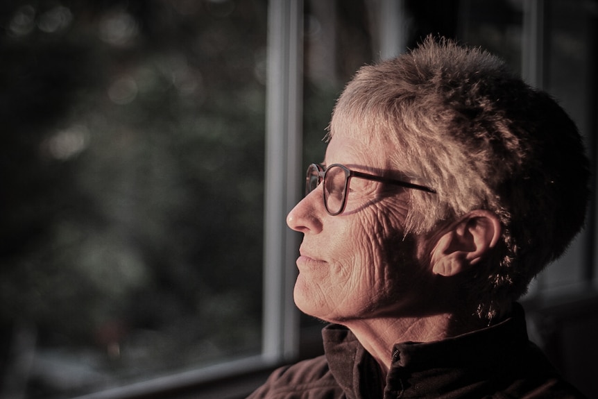 A woman with grey hair and glasses looks out the window smiling 