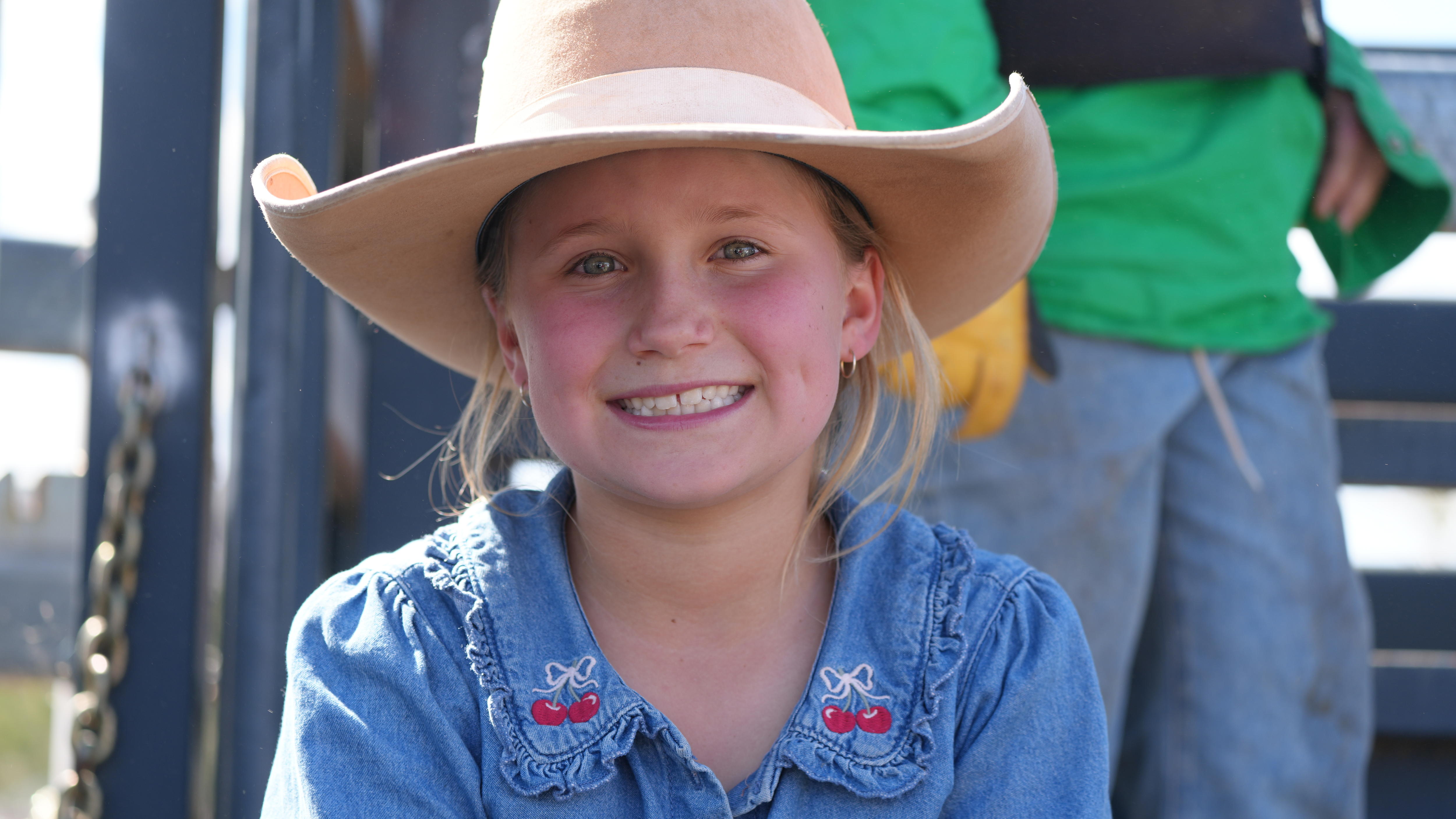 A young girl in a cowboy hat grins