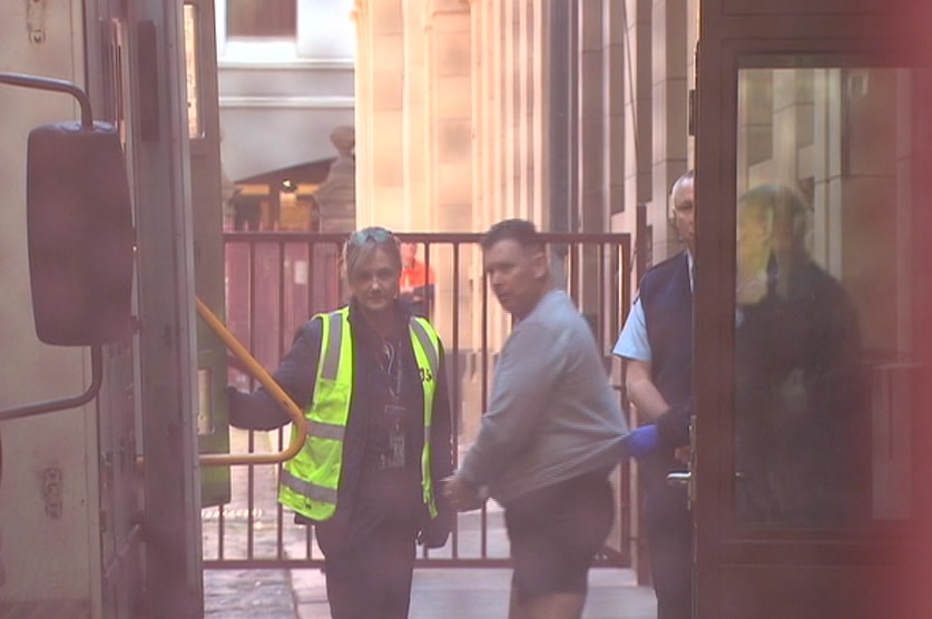 A man in shorts being escorted by security officials.