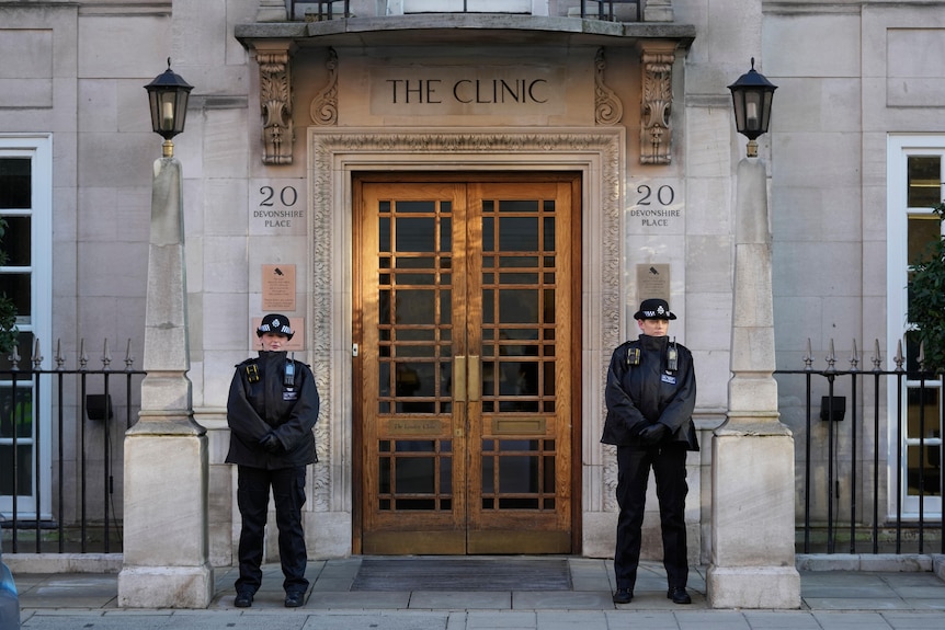 A wide photo of two female police officers standing outside the entrance to a building with 'The Clinic' written above its door
