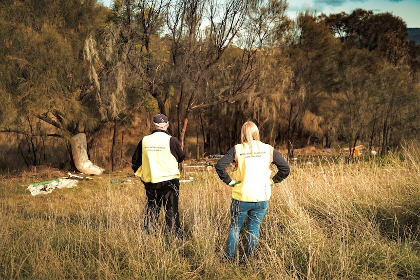 Two people survey rubbish in a field