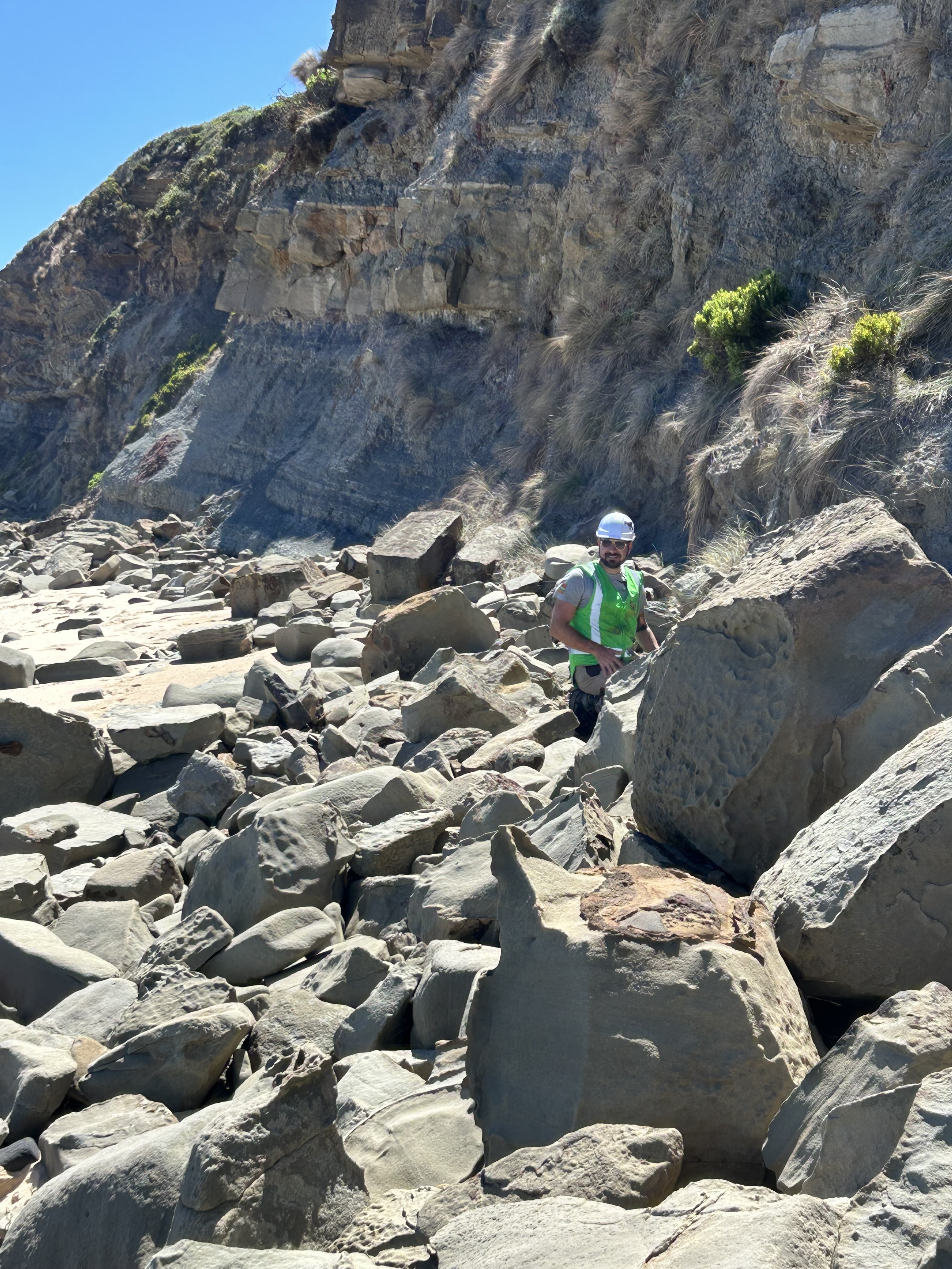 Man in hi-vis gear standing among coastal rocks.