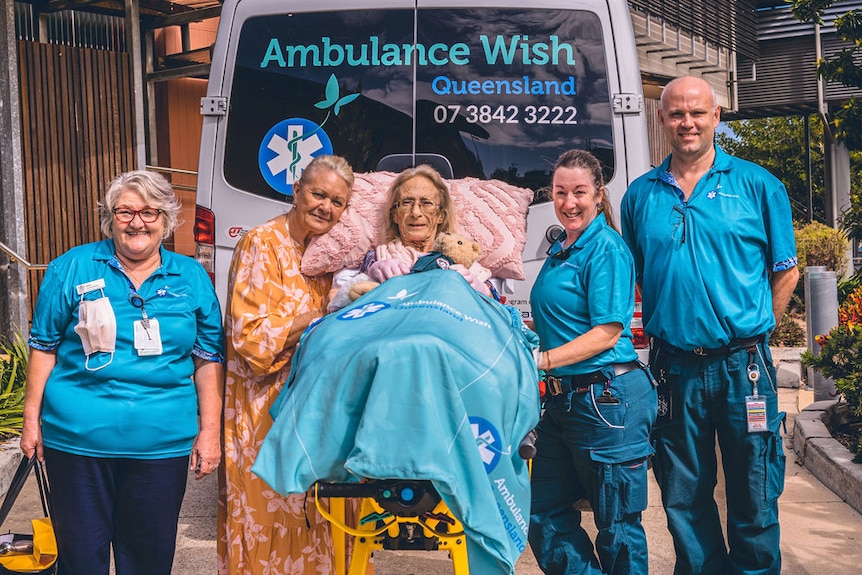 A medical team with an ill patient, standing together next to an ambulance.