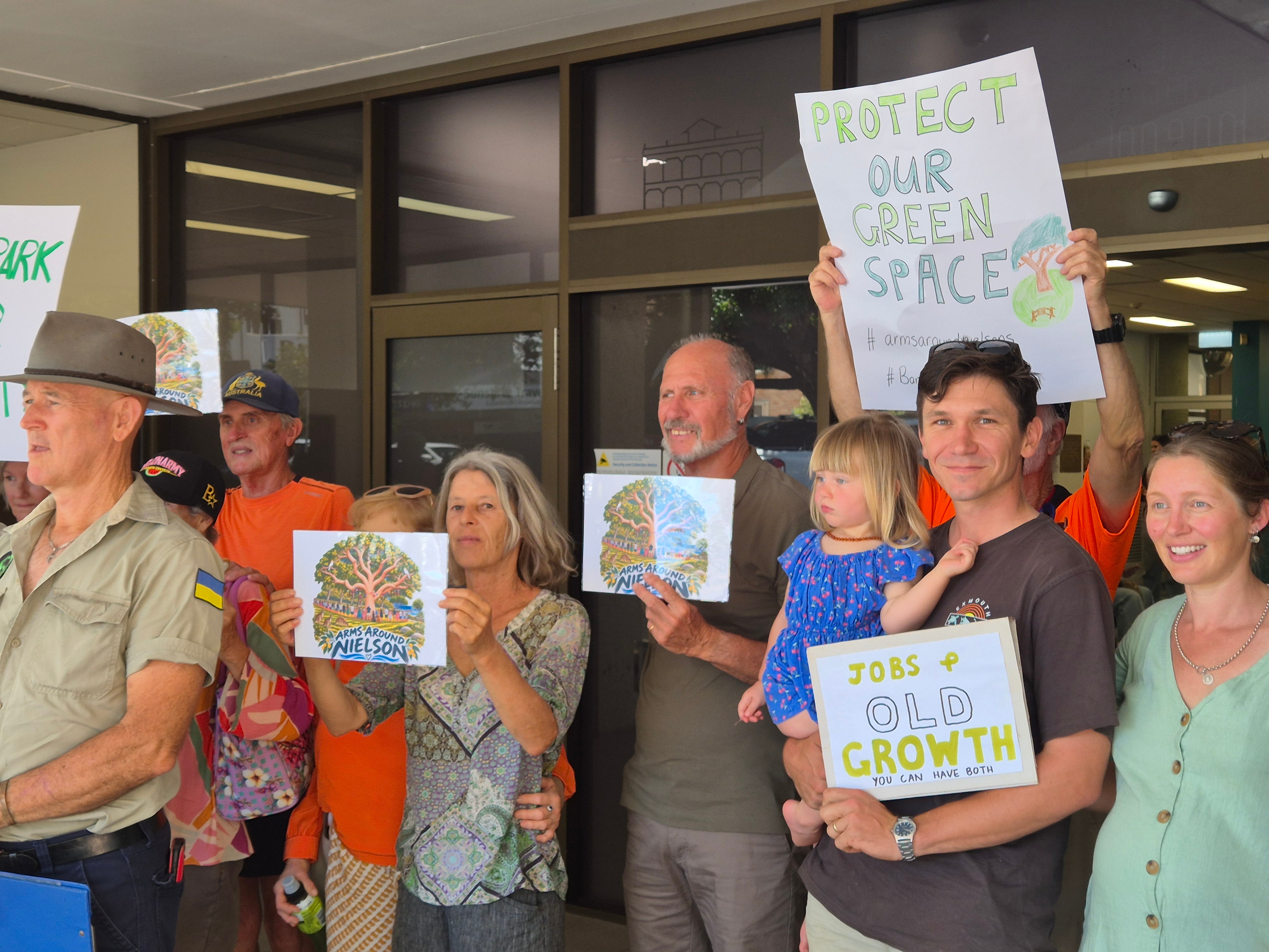 A group of people gathered outside the bundaberg council meeting holding protest signs.