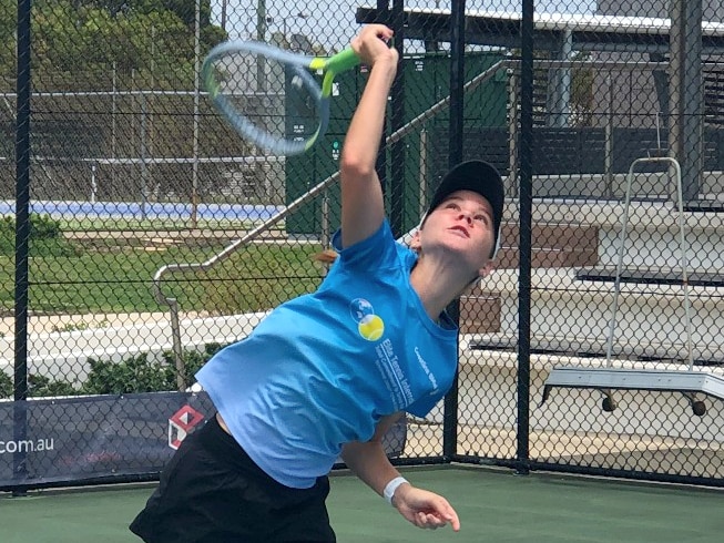 A teenage girl wearing blue t-shirt, shorts, cap, hits a serve on the tennis court.