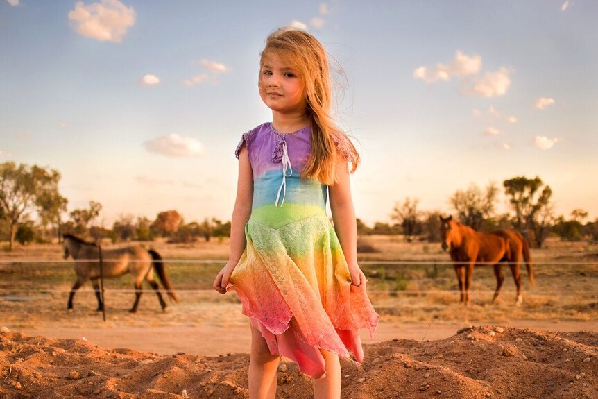 A little girl poses in her favourite dress in the soft afternoon light in the horse paddock