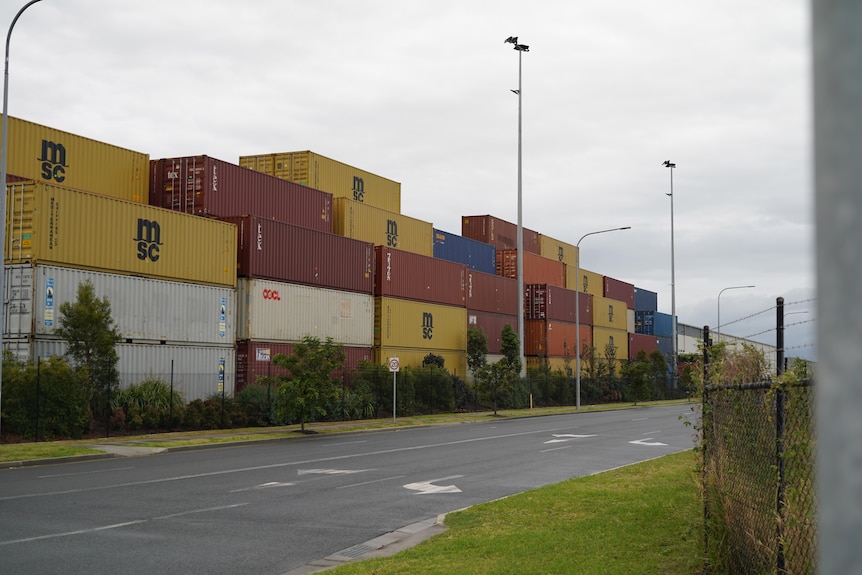 A row of stacked shipping containers by the side of a road.