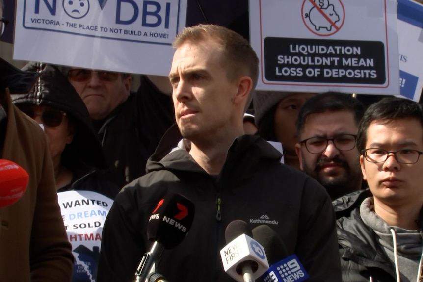 Richard Davis, a man with short light hair, looks angry as he talks to media at a protest.