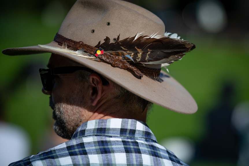 A man wears feathers and an Aboriginal flag badge on his hat