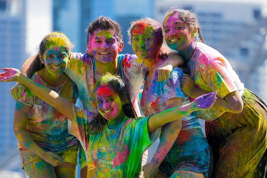 Five young people in white clothing covered with bright coloured powders.